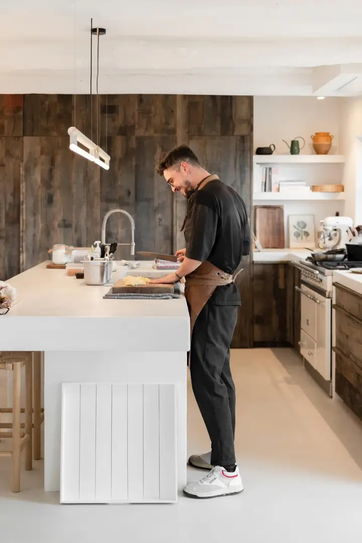 Homme préparant un plat dans une cuisine ouverte en bois sombre avec un îlot blanc